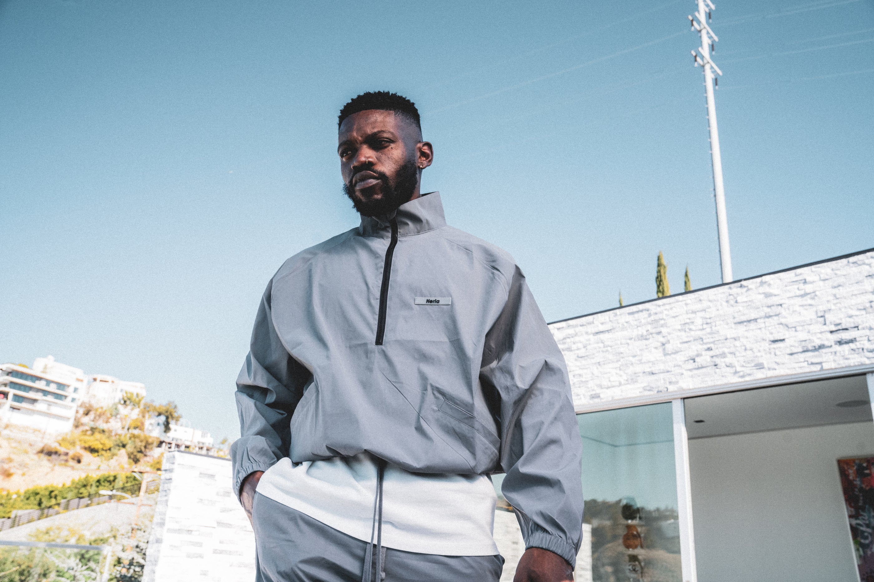 Male model pose in the hERIA 3m Reflective Jacket , 3M reflective shorts and white tee under a sunny blue sky.