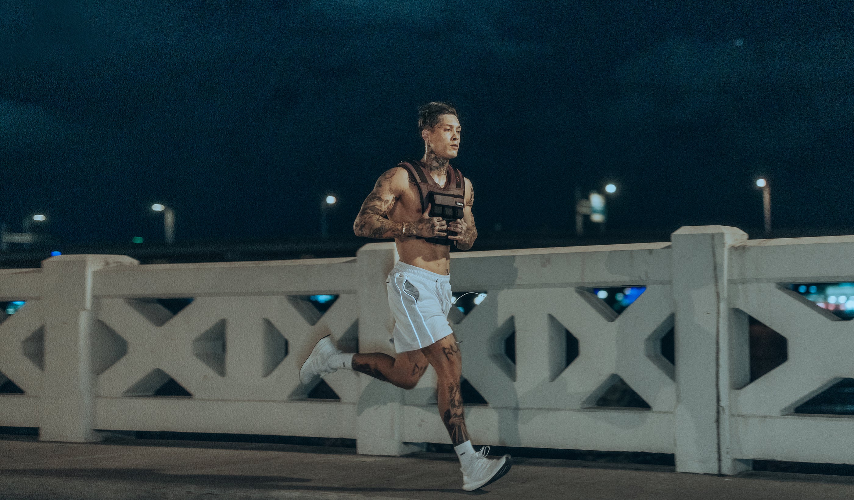 Chris Heria running at night time while wearing the Iridescent 28lb weighted vest, Heria Mesh shorts in  white, heria white crew socks and running shoes.