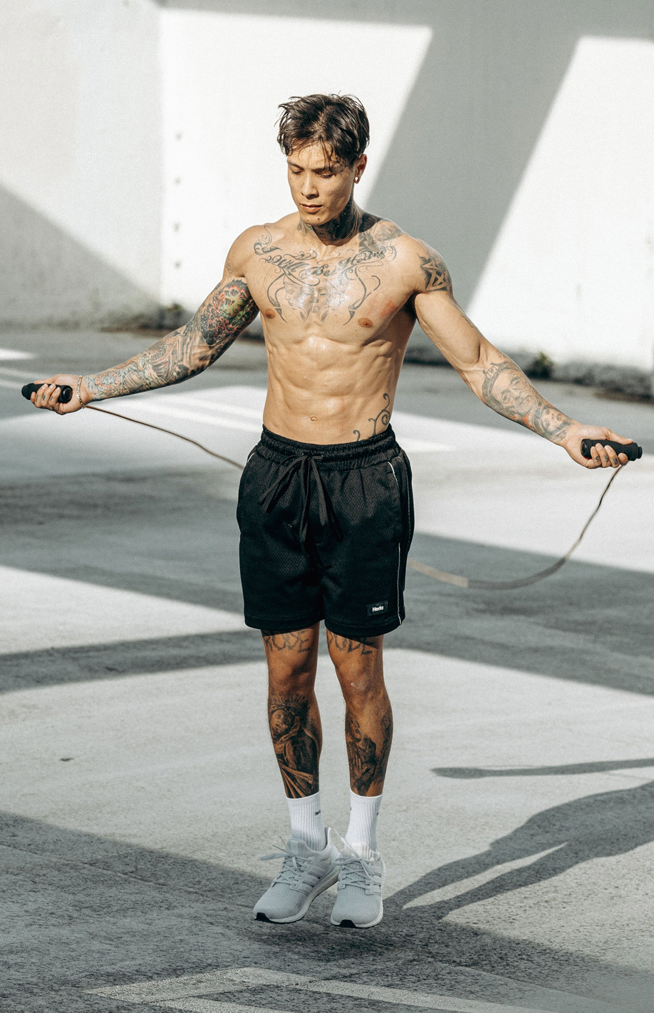 Chris Heria exercises with a jump rope while wearing black Heria Mesh Shorts with 3M Reflective Piping.